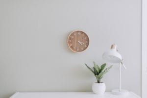 Picture of clock above white desk with plant and lamp